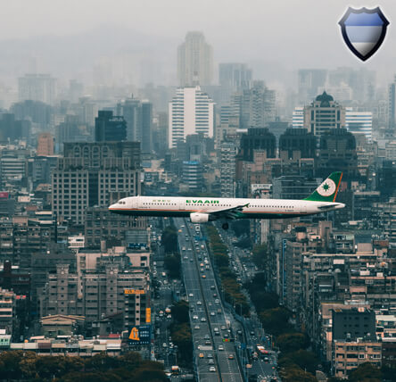 An airliner flying through a city surrounded by tall buildings